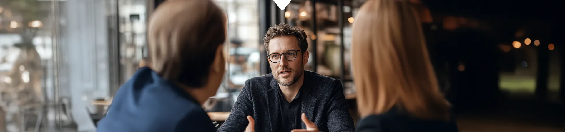 Geschäftsgespräch in einem modernen Café mit drei Personen, die eine Diskussion führen.