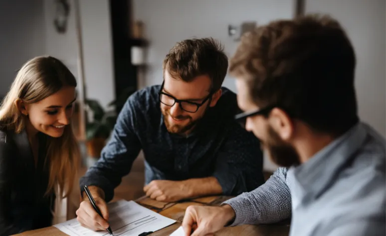 Drei Personen diskutieren und unterschreiben Dokumente an einem Tisch